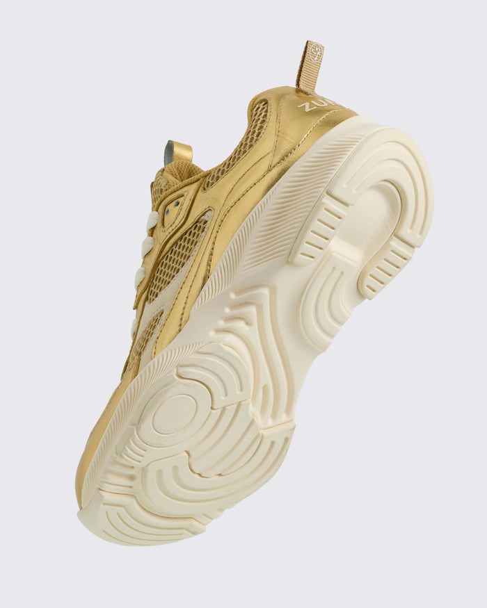 Sole view of the gold Zumba sneaker with white sole on a light background.