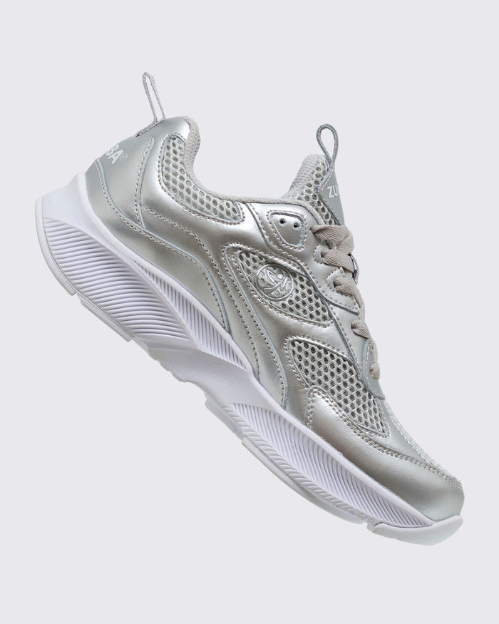 Silver Zumba athletic shoe, shown at a right angle and with a small silver Zumbito.