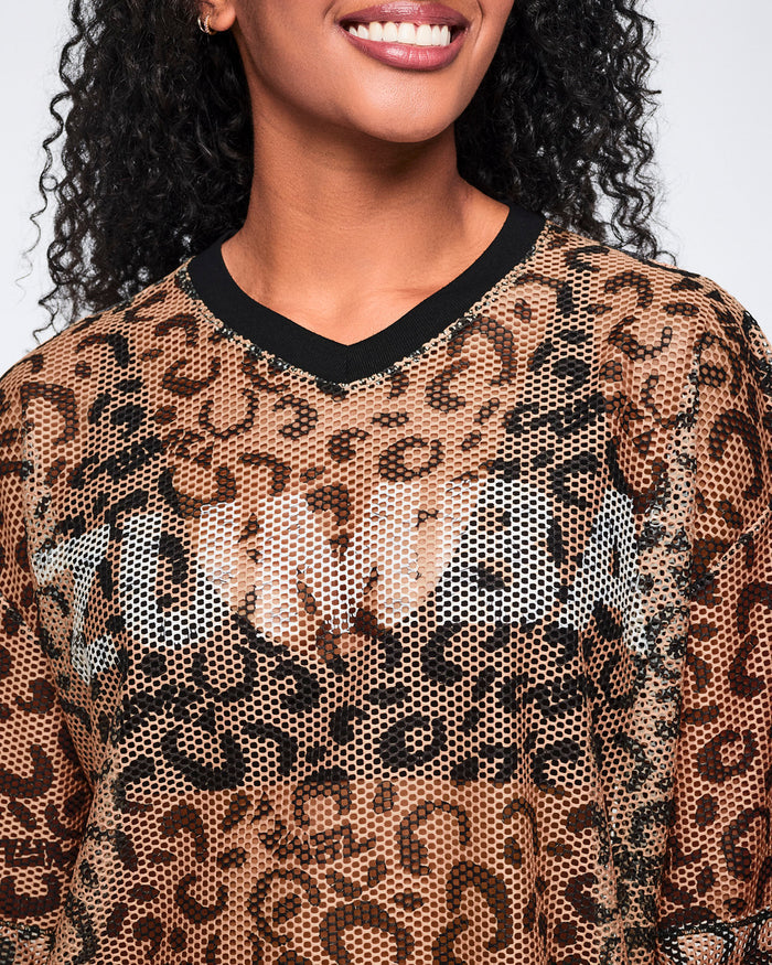 Close-up of a tan leopard-print mesh top with black abstract spots and a black V-neck collar, shown on a smiling female model.