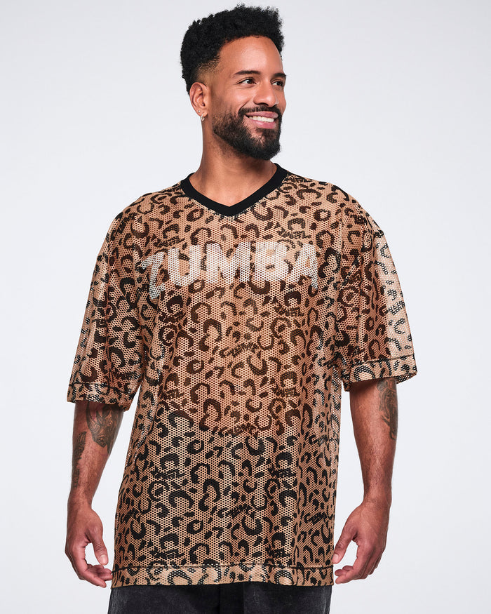 Tan leopard-print mesh top with black abstract spots, a black V-neck collar, oversized fit, and elbow-length sleeves, shown on a smiling male model wearing black long shorts.