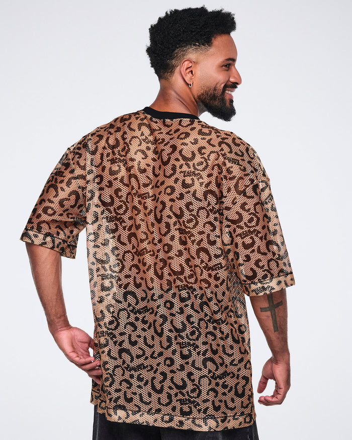 Tan leopard-print mesh top with black abstract spots, a black V-neck collar, oversized fit, and elbow-length sleeves, shown from the back on a smiling male model wearing black shorts.