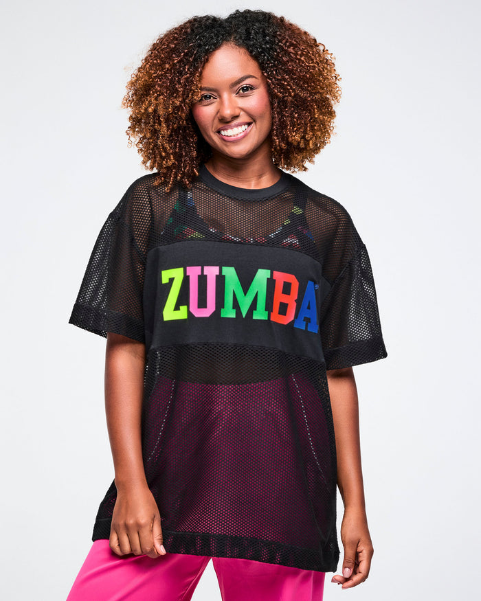 Female model wearing a black Zumba mesh top with colorful Zumba letters across the chest, on a plain background.