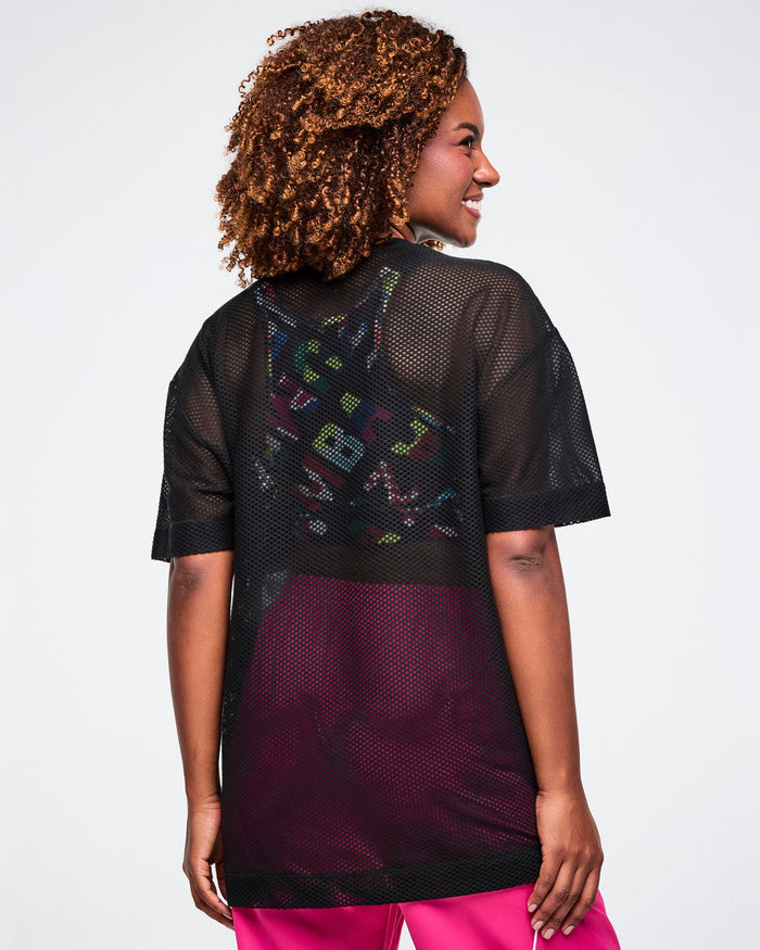 Back view of a female model wearing a black Zumba mesh top on a plain background.