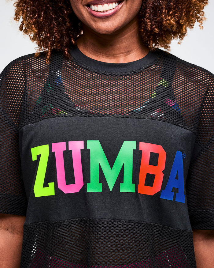 Close-up of a female model wearing a black Zumba shirt with colorful letters on a plain background.