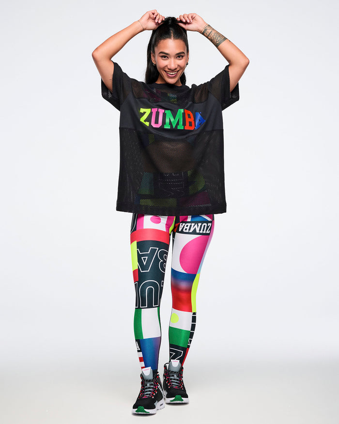 Female model wearing a black mesh Zumba top and colorful leggings on a white background.
